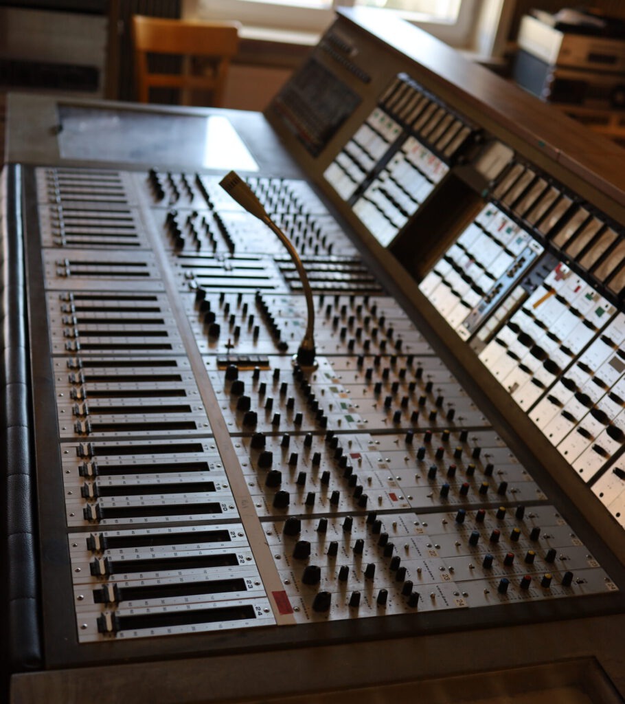 Analoges Mischpult im MPS-Studio in Villingen-Schwenningen mit vielen Fadern, Drehreglern, Pegelanzeigen und einem Schwanenhalsmikrofon.